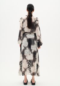 Vestido maxi de tela transparente con un patrón floral en tonos suaves de rosa, negro y crema. Mangas largas y cintura ajustada.