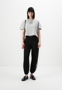 Grå, kortermet T-skjorte med en subtil logo, kombinert med sorte, avsmalnende joggebukser med hvite detaljer, og blanke svarte loafers.
