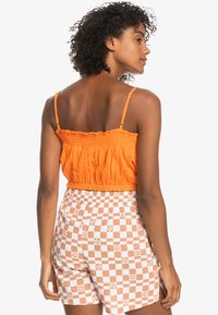 Orange smocket crop top med tynde stropper, parret med hvide shorts med ferskenfarvet ternet mønster og blomstrede accenter.
