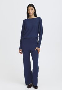 Námornícky modrý pletený outfit so voľným dlhým rukávom a širokými nohavicami. Hladká textúra, minimalistický dizajn a elastický pás.