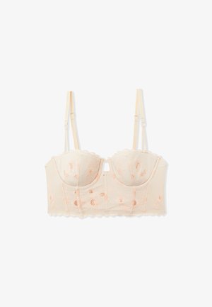 Lace bralette in light nude with peach floral embroidery, structured cups, and scalloped edges. Adjustable straps and hook closure at back.