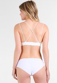 Λευκό μπικίνι σετ με απλό σχέδιο, διαθέτει λεπτές δι�ασταυρούμενες τιράντες στο τοπ και αντίστοιχο κάτω μέρος, και τα δύο με λεία υφή.