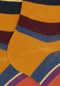 Calze colorate impilate, lavorate a maglia, con righe orizzontali in giallo senape, blu, bordeaux, viola e arancione.