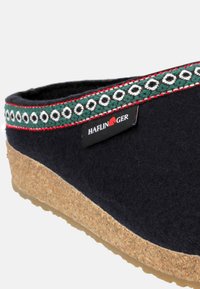 Svart filtträsko med korksål, dekorativ grön och vit flätad trim och en röd accent. Har "Haflinger"-logotypen.