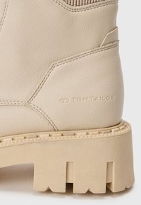 Beige ankelstøvler laget av teksturert skinn, med en kraftig såle med dype spor og preget "TOM TAILOR"-logo på siden.