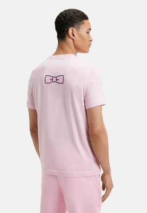 T-shirt rose à manches courtes en tissu doux, avec un motif de nœud noir brodé dans le haut du dos.