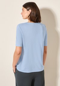 Camiseta de manga corta color azul claro, hecha de una tela suave y texturizada. Presenta un cuello redondo y un ajuste relajado, con un dobladillo recto y sin adornos.