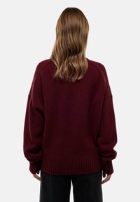 Pull oversized bordeaux avec ourlet et poignets côtelés, fabriqué à partir d'un tissu doux et texturé, présentant des épaules tombantes et une coupe décontractée.