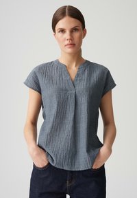 Maglietta azzurra chiara a maniche corte con un tessuto testurizzato e stropicciato. Presenta un collo a V e una vestibilità rilassata, abbinata a pantaloni in denim scuro.