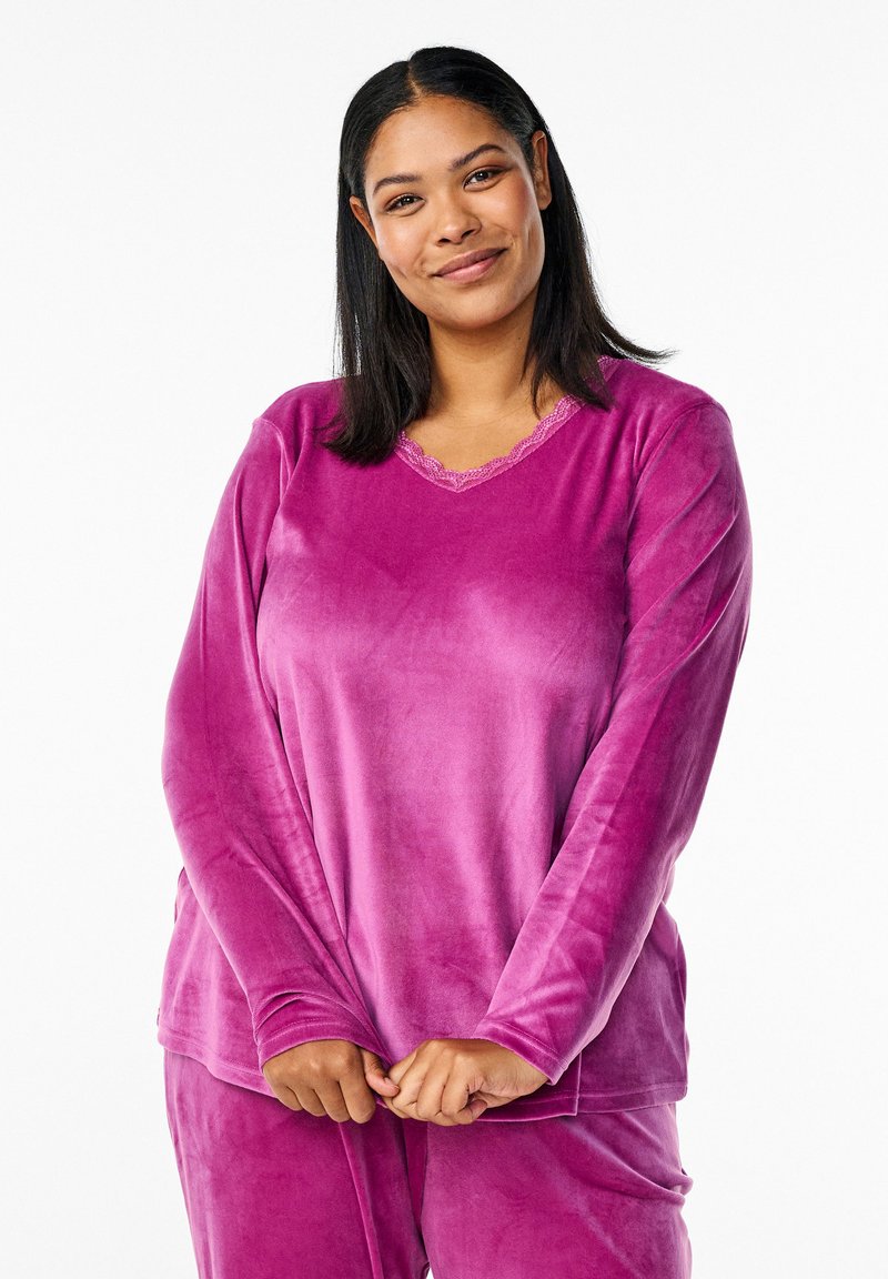 Top lungo in velour rosa con maniche lunghe, scollo a V, rifiniture in pizzo e una texture morbida, abbinato a pantaloni coordinati in una vestibilità rilassata.