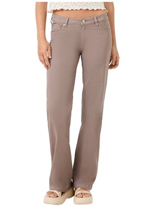 Kobieta w taupe spódnicach z szerokimi nogawkami i wysokim stanem z przednimi kieszeniami oraz beżowych sandałach na platformie, stojąca na białym tle.