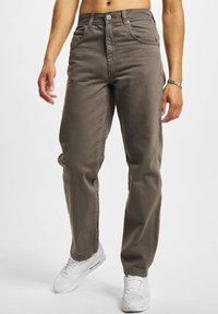 Pantaloni din denim maro cu croi drept, având bucle pentru curea, închidere cu nasture și două buzunare frontale. Purtați cu adidași albi.