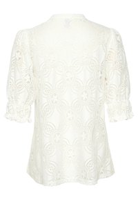 Haut en dentelle blanc cassé avec des motifs floraux, manches bouffantes et poignets froncés élastiques. Vue de dos affichée, mettant en valeur une texture intricate.