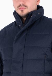 Giacca imbottita blu navy con colletto alto, caratterizzata da texture trapuntata orizzontale e zip frontale, decorata con dettagli a bottoni a scatto.