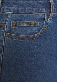 Mörkblå denimjeans med en närbild, med orange sömmar och en liten bakficka. Mjukt tyg, robust material.
