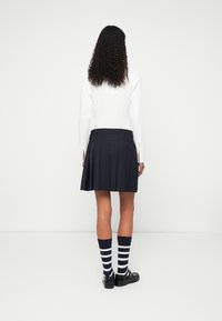 Σκούρα μπλε πλισέ φούστα συνδυασμένη με λευκή μακριά μπλούζα, μαύρα παπούτσια και κάλτσες με navy και λευκές ρίγες. Απαλή ύφανση και έντονες πτυχές.