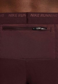 Nike Running viininpunaiset shortsit, joissa on teksturoitu pinta, musta vetoketjullinen tasku ja vyötärö, johon on painettu "NIKE RUNNING."