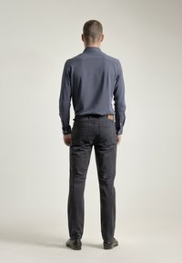 Camisa de manga larga gris oscuro con puños de botón, combinada con pantalones negros con bolsillos traseros y un detalle de cuero en la cinturilla.