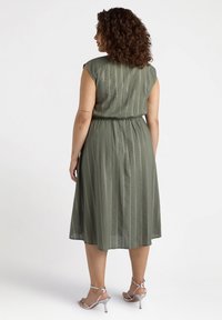 Olivengrünes Kleid mit lässiger Passform, Kurzärmeln, elastischem Bund und vertikalen Streifen. Strukturierter Stoff mit subtiler Eleganz und mittellangem Saum.