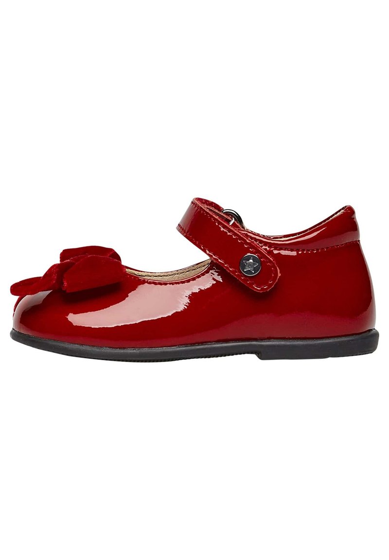 Zapato Mary Jane de charol rojo con punta redonda, correa de velcro y detalle de lazo de tela rojo oscuro en la parte delantera. Suela plana de goma negra.
