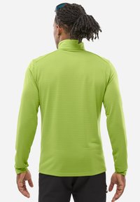 Pull-over à manches longues de couleur vert vif, fabriqué en tissu texturé avec un motif en damier. Il présente un col haut et des manches ajustées.