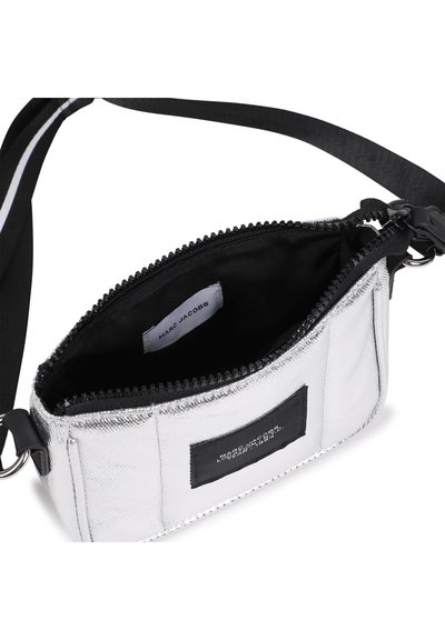 Ασημένια μεταλλική τσάντα ώμου με φερμουάρ στην κορυφή, μαύρη υφασμάτινη επένδυση, ρυθμιζόμενο λουρί και ετικέτα με λογότυπο στο πλάι. Συμπαγές ορθογ ώνιο σχήμα.