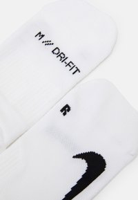 Hvide Nike sokker med sort "M // DRY-FIT" tekst på den ene sok og "R" på den anden, med ribbet tekstur og et markant Nike swoosh-design.