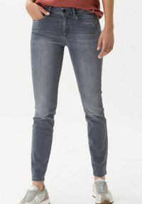 Jeans skinny grigi sbiaditi realizzati in denim, con cinque tasche, chiusura con bottone e passanti per cintura, abbinati a sneakers grigie chiare.