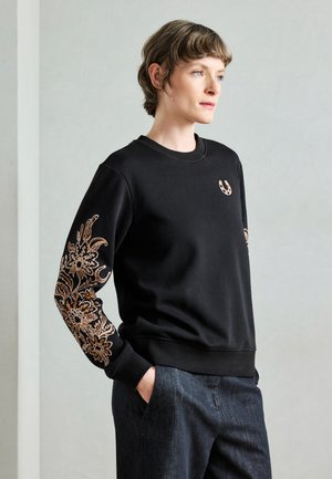 Czarna bluza z długimi rękawami ozdobiona misterną, brązową kwiatową haftą oraz małym logo na piersi. Materiał o fakturowanej strukturze.