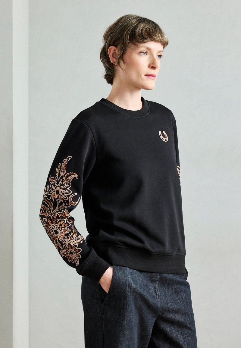 Μαύρο φούτερ με μακριά μανίκια και περίτεχνη μπρούντζινη κεντητή διακόσμηση με λουλούδια, καθώς και μικρό λογότυπο στο στήθος. Υφασμάτινη υφή.