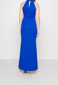 Niebieska, dopasowana sukienka na halter z otworem w kształcie łezki na plecach, w długości do ziemi, o gładkiej fakturze. Akcentowana minimalnymi elementami metalowymi.