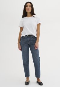 T-shirt bianco a maniche corte abbinato a jeans in denim blu scuro a vita alta e ballerine nere, caratterizzato da un taglio dritto e un design classico.