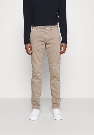 Pantalones chinos beige con pernera recta, textura sutil y diseño de cinco bolsillos. Combinados con zapatillas blancas y un suéter navy.