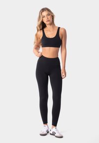 Sujetador deportivo negro y leggings de talle alto hechos de una tela elástica; textura suave; combinados con zapatillas deportivas blancas y grises.