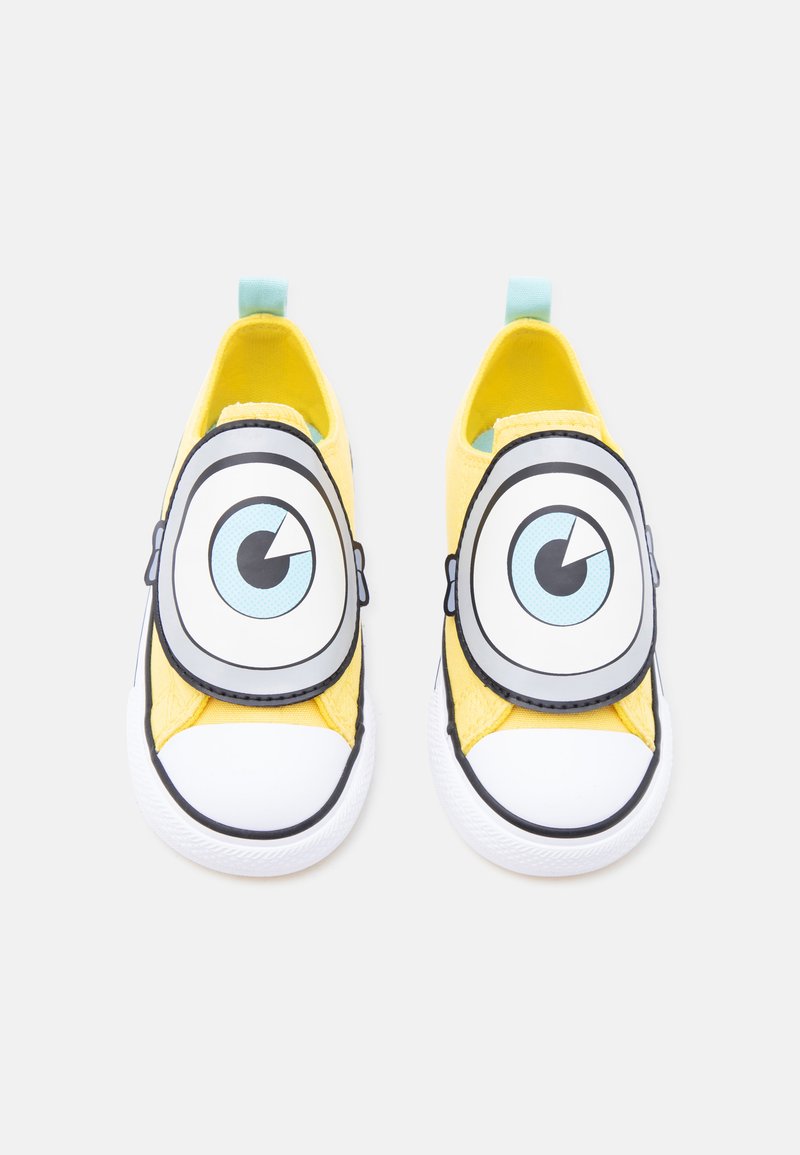 Paire de chaussures jaunes à enfiler pour enfants avec de grands yeux de dessin animé sur le dessus et des embouts en caoutchouc blanc.