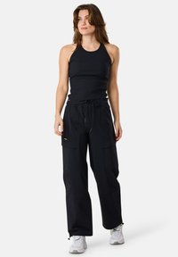 Musta ribbattu tank-top yhdistettynä löysiin mustiin cargo-housuihin. Housuissa on sivutaskut ja joustava vyötärö, joka säätää istuvuutta.