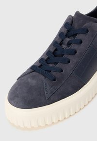 Sneaker in suede blu navy con suola spessa bianca rigata e lacci blu abbinati su uno sfondo chiaro e semplice.