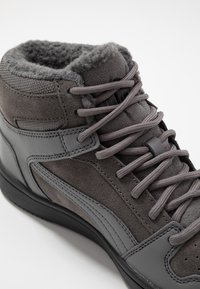 Chaussure montante grise en daim et matériau synthétique, avec une surface texturée, un col rembourré et des lacets ronds, montée sur une semelle noire.