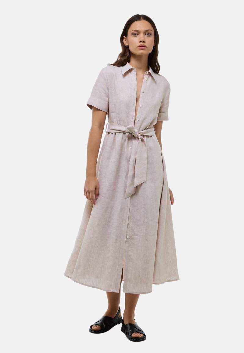 Robe chemise en lin beige à manches courtes, boutons sur le devant, taille cintrée avec ceinture nouée, et jupe évasée. Portée avec des sandales noires à enfiler.