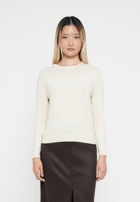 Cream-colored long-sleeve sweater with a ribbed hem and subtle bead accents along the neckline, made of lightweight knit material.
