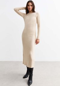 Abito a coste, a maniche lunghe, beige con silhouette aderente e spacchi laterali, abbinato a stivali neri al ginocchio.