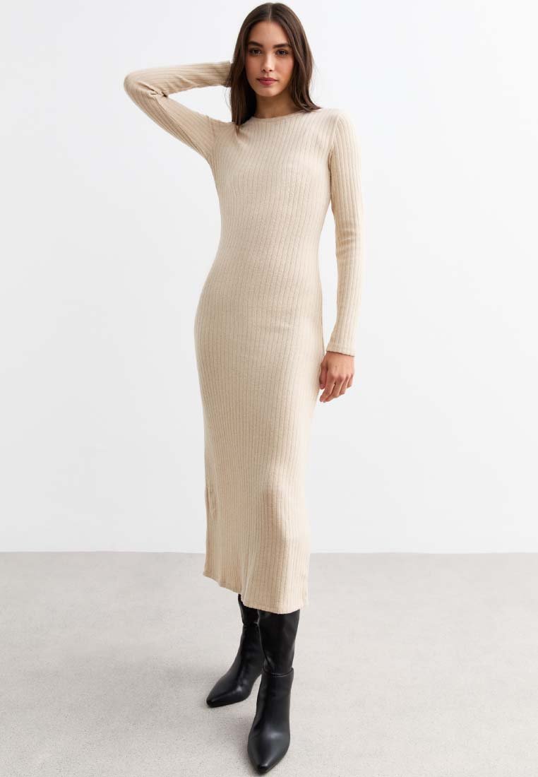 Abito a coste, a maniche lunghe, beige con silhouette aderente e spacchi laterali, abbinato a stivali neri al ginocchio.