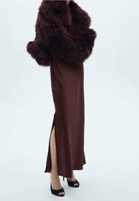 Bordeaux nep bont schoudergedeelte gecombineerd met een bruin satijnen maxi-jurk met een hoge split en zwarte openhakken. Over het geheel een gladde textuur.