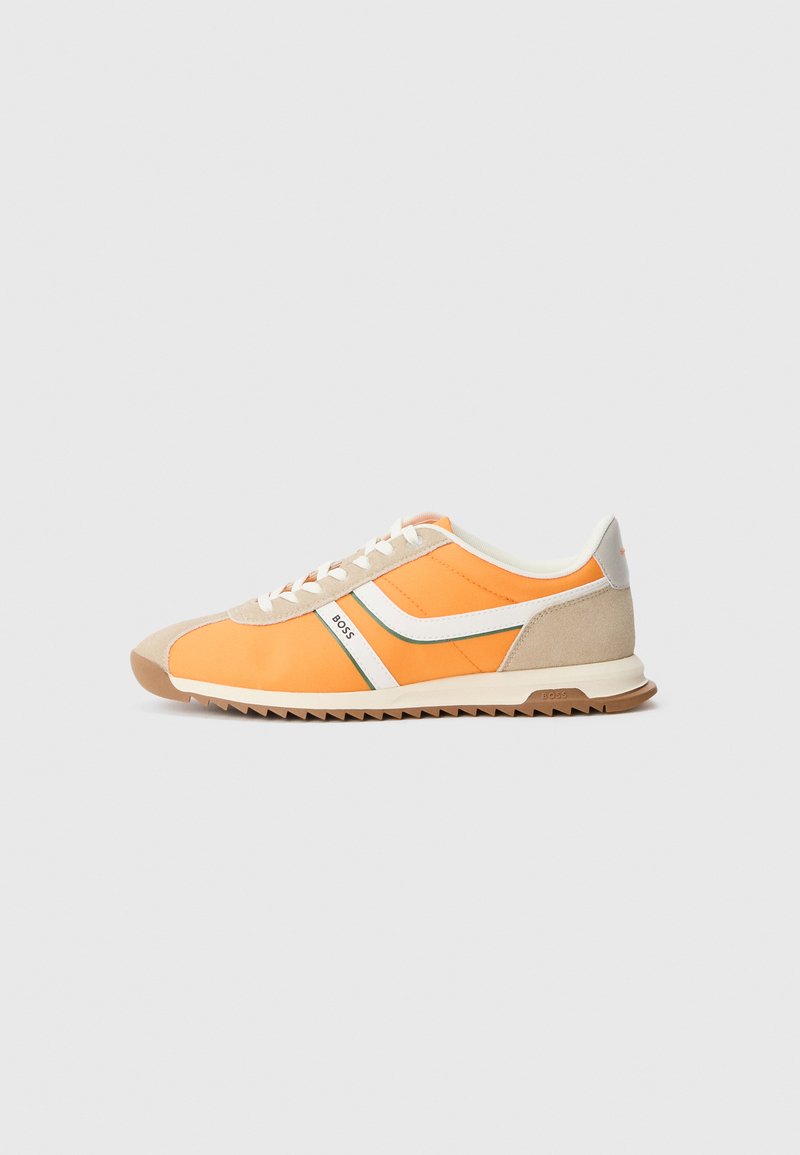 Sneaker mit einem orange-beigen Mesh-Obermaterial, weißen Akzenten, grünen Linien und einer strukturierten Gummisohle. Mit abgerundetem Zehenbereich und Schnürdesign.