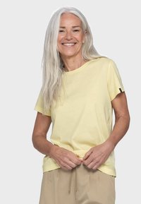 Gelbes Kurzarm-T-Shirt aus einem weichen, leichten Stoff. Rundhalsausschnitt, mit einem Logo-Tag am linken Ärmel. Glatte Textur.