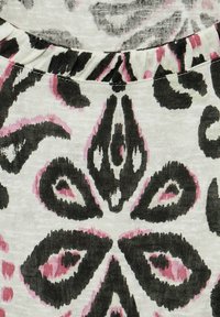 Tejido con un patrón floral en negro y rosa sobre un fondo crema, con una textura de tejido y detalle de cuello con volantes.