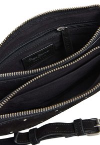 Sac en daim noir à bandoulière avec plusieurs compartiments, fermetures zippées et une fermeture éclair en métal argenté. L'intérieur est doublé de tissu noir.
