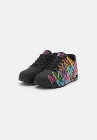 Schwarze Sportschuhe mit bunten Herzdesigns in Pink, Grün, Blau und Orange. Strukturiertes Obermaterial und Gummisohle für guten Halt.
