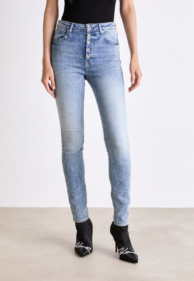 Högmidjade blå jeans med en femknappsförslutning, lätt slitage och en åtsittande design. I kombination med svarta spetsiga ankelskor.