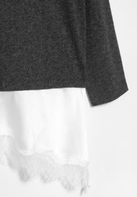 Grå striktrøje med et hvidt underlag, der har en dekorativ blonderkant ved kanten. Stoffet er blødt med en glat tekstur.